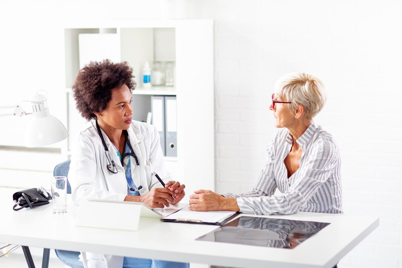 Female provider talking with a mature woman patient at a desk in a clinic