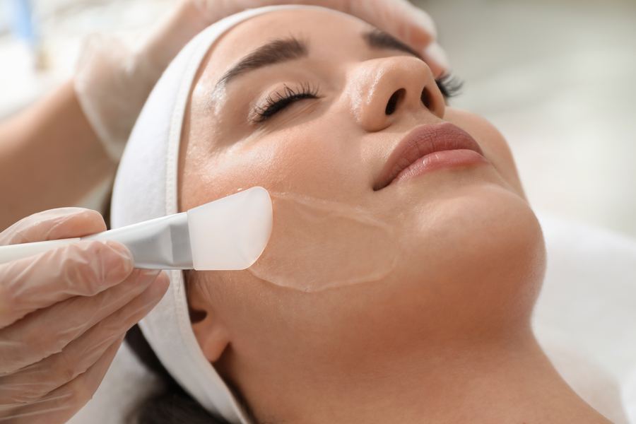 Esthetician applying a chemical peel solution to a patient's cheek