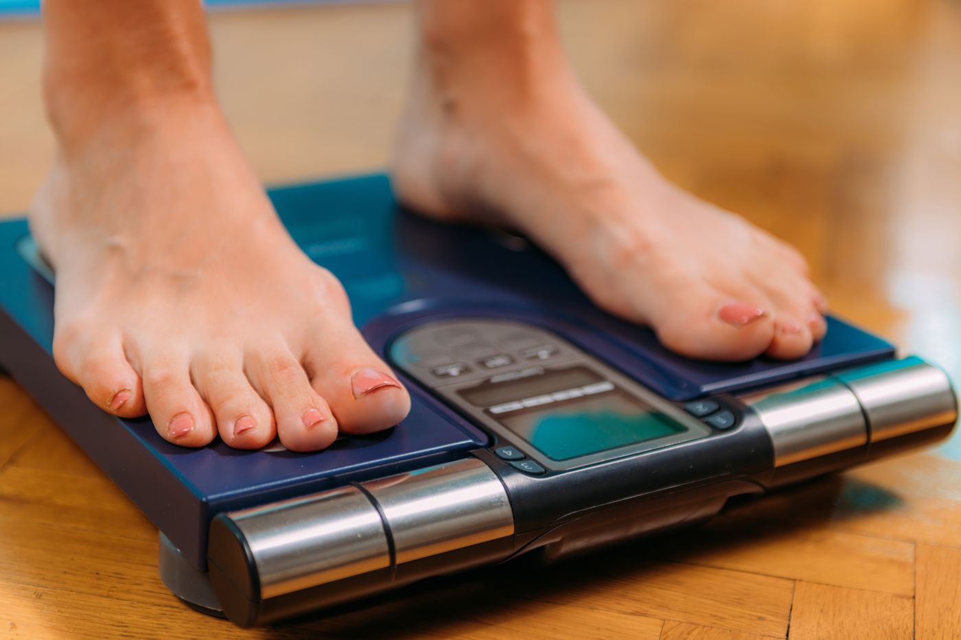 Bare feet on a body composition scale with hand electrodes and a digital display