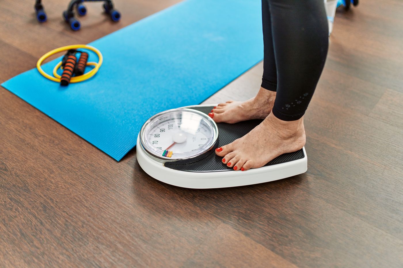 Woman standing barefoot on a bathroom scale beside an exercise mat