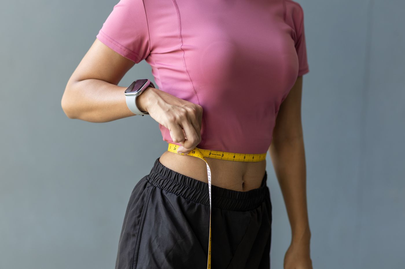 Woman measuring her waist with a tape measure while wearing a smartwatch